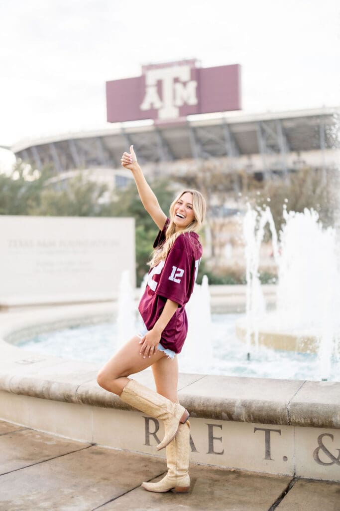 Adeline in her 12th Man jersey celebrating graduation with champagne pop at the Association of Former Students fountain