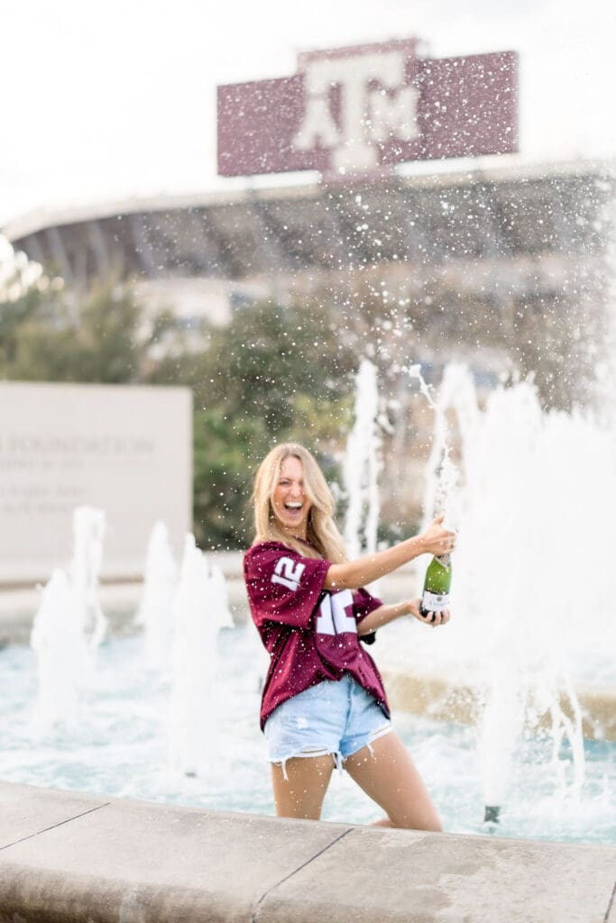 Adeline in her 12th Man jersey celebrating graduation with champagne pop at the Association of Former Students fountain