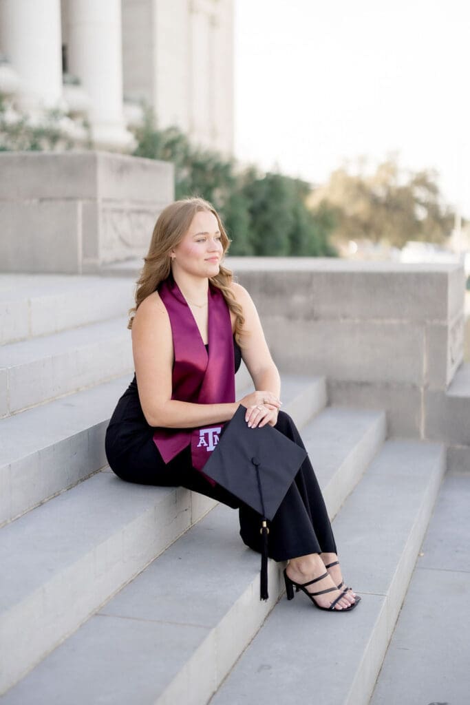 TAMU senior photos at the Admin Building featuring Grace smiling on the steps in her maroon stole