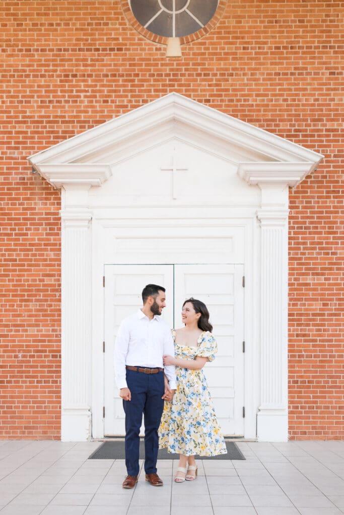 Engaged couple posing near St. Mary’s Catholic Center church entrance in College Station
